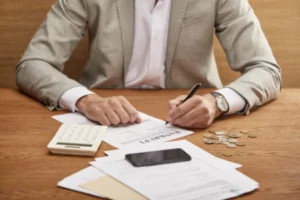 Businessperson reviewing financial documents and signing bankruptcy papers with coins, calculator, and phone on the desk.
