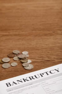 Bankruptcy form and scattered coins on a wooden table, representing financial challenges and filing considerations.