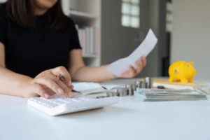 Woman calculates finances with bill, coins, and piggy bank—symbolizing Chapter 13 plan modification due to income changes.