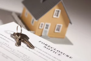 House keys on top of a foreclosure notice with a model house in the background, symbolizing home foreclosure risk.